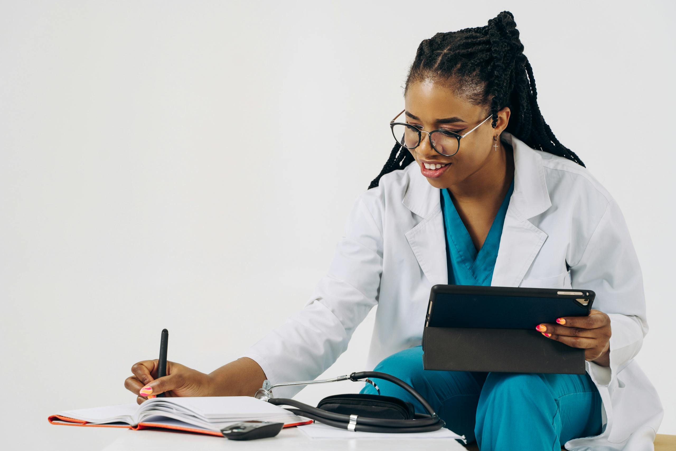 Smiling female doctor in scrubs using tablet and taking notes in a healthcare setting.